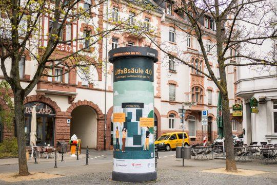 Die klassische, seit mehr als 170 Jahren bekannte Litfaßsäule erfährt eine Renaissance als Warnmultiplikator. Die Idee: Wenn bei einem langanhaltenden Stromausfall andere Kommunikationsmedien wie Mobilfunk, Internet oder Fernsehen ausfallen, kann die energieautarke Litfaßsäule 4.0 Menschen weiterhin informieren. Am Donnerstag (4.3.) nahmen das LOEWE-Zentrum emergenCITY, die Technische Universität Darmstadt und das Medienhaus Ströer den in einer gemeinsamen Forschungskooperation entstandenen Prototypen auf dem Riegerplatz in Darmstadt in Betrieb. Neben der technischen Erprobung sollen wissenschaftliche Untersuchungen im Anschluss zeigen, wie die Darmstädterinnen und Darmstädter die Warnsäule wahrnehmen. Im Bild: Installation der Säule auf dem Darmstädter Riegerplatz am 2. April 2024. Foto: Sascha Mannel